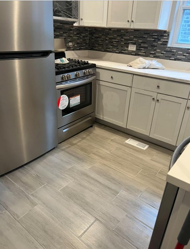 kitchen featuring light countertops, appliances with stainless steel finishes, visible vents, and decorative backsplash