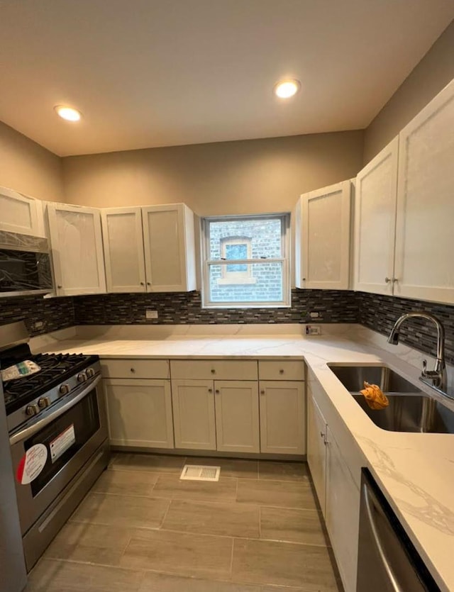 kitchen with light stone counters, recessed lighting, a sink, appliances with stainless steel finishes, and backsplash