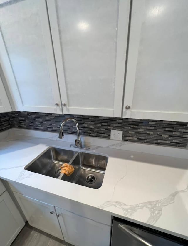 room details with white cabinets, decorative backsplash, light stone countertops, stainless steel dishwasher, and a sink