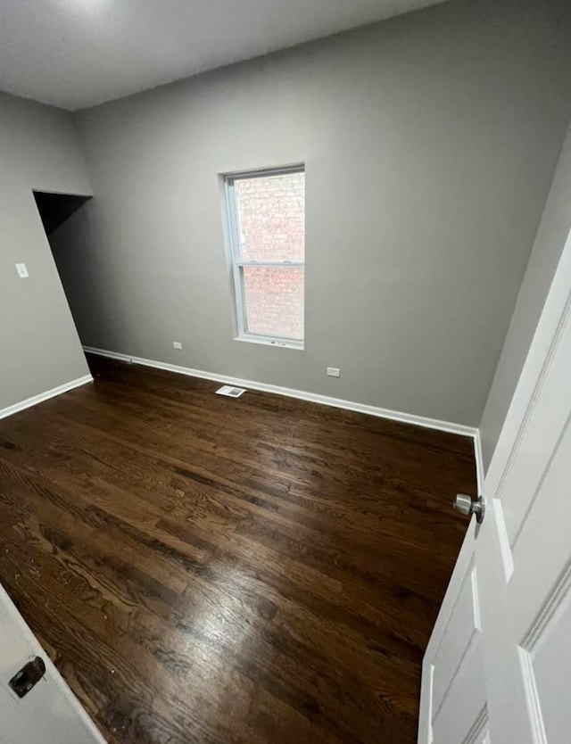 unfurnished room with dark wood-style flooring, visible vents, and baseboards