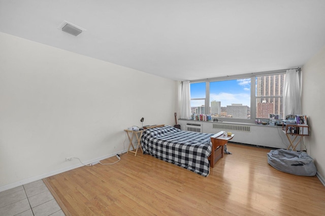 bedroom with a view of city, wood finished floors, visible vents, and baseboards