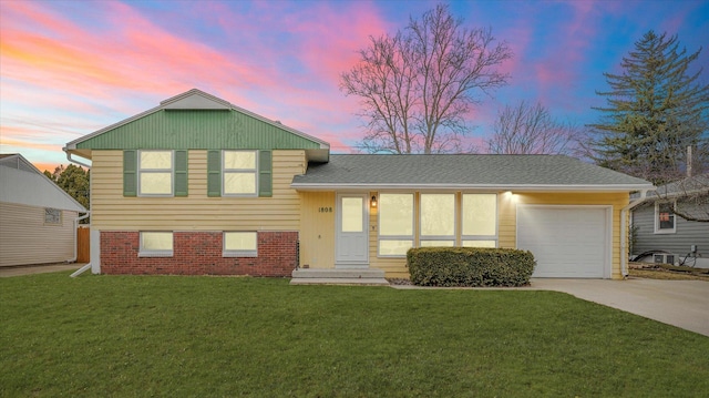 split level home featuring an attached garage, brick siding, driveway, a yard, and roof with shingles