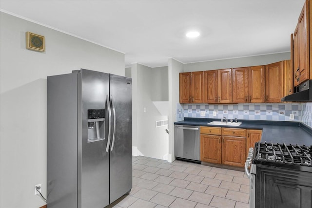 kitchen featuring brown cabinetry, dark countertops, appliances with stainless steel finishes, under cabinet range hood, and a sink