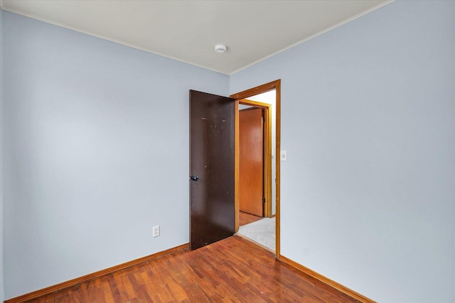 empty room featuring crown molding, wood finished floors, and baseboards