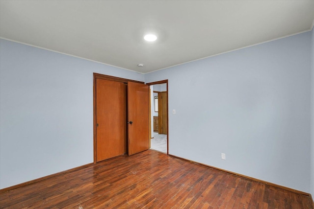 unfurnished bedroom with baseboards, a closet, ornamental molding, and hardwood / wood-style floors