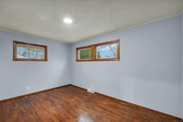 unfurnished room featuring a textured ceiling, dark wood-style flooring, visible vents, and baseboards