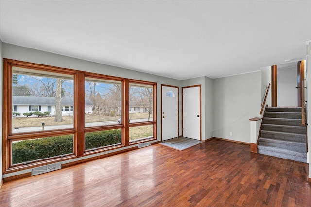 unfurnished living room with visible vents, stairway, baseboards, and wood finished floors