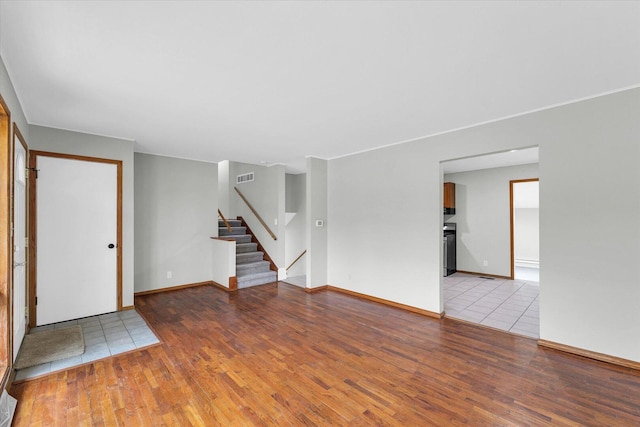 unfurnished living room featuring stairs, wood finished floors, visible vents, and baseboards