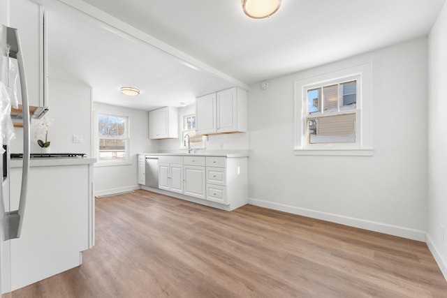 kitchen with light wood finished floors, baseboards, white cabinets, light countertops, and a sink