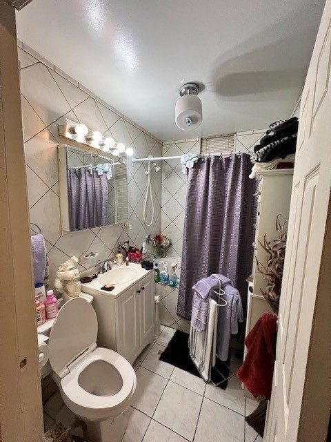 bathroom with toilet, vanity, a shower with curtain, tile patterned floors, and tile walls