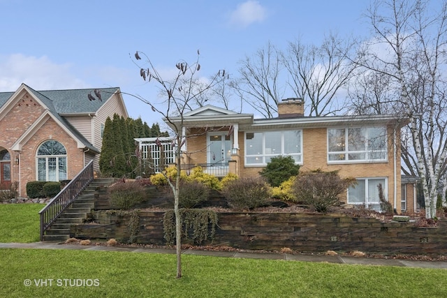 view of front of home with a front yard, stairs, a chimney, and brick siding