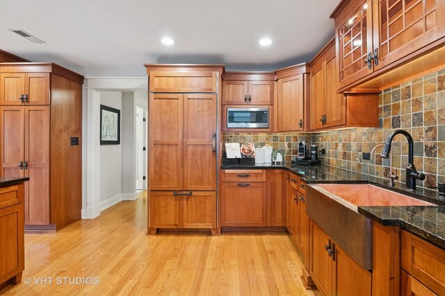 kitchen featuring built in appliances, brown cabinetry, a sink, and visible vents