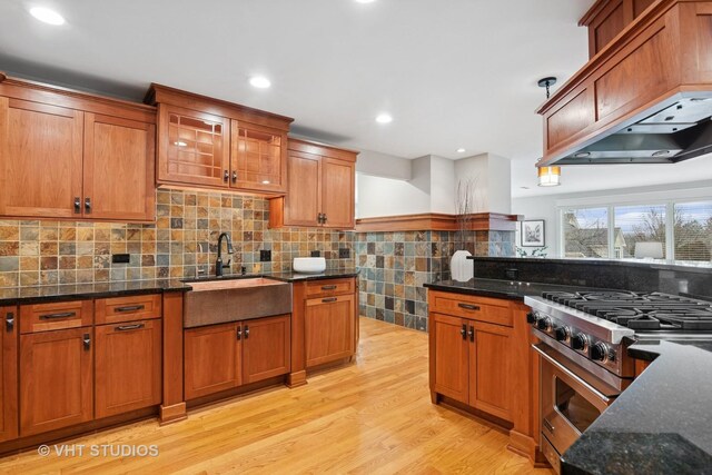 kitchen with dark stone counters, brown cabinets, high end stove, light wood-style floors, and a sink