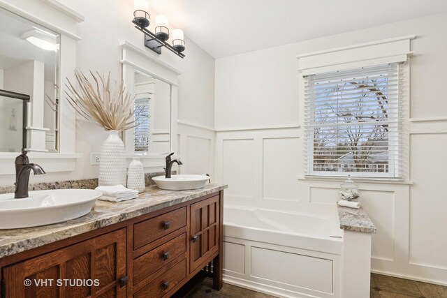 full bath featuring double vanity, a sink, a bath, and a decorative wall