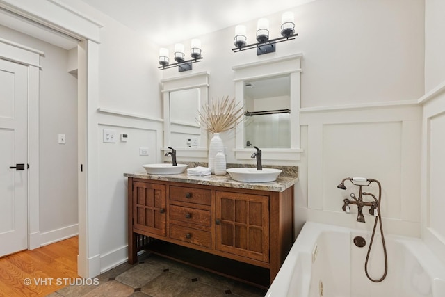 full bath featuring double vanity, a bathtub, a decorative wall, and a sink