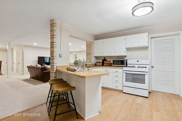 kitchen featuring decorative columns, a breakfast bar area, white gas range, stainless steel microwave, and butcher block countertops