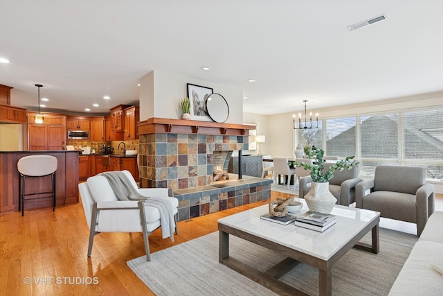 living area with visible vents, light wood-style flooring, a fireplace, a chandelier, and recessed lighting