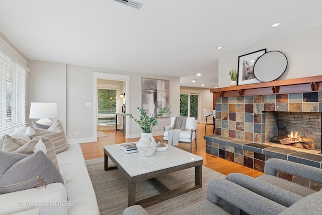 living room featuring baseboards, visible vents, a tiled fireplace, wood finished floors, and recessed lighting