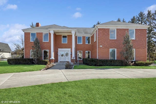 greek revival inspired property with brick siding, a chimney, and a front yard