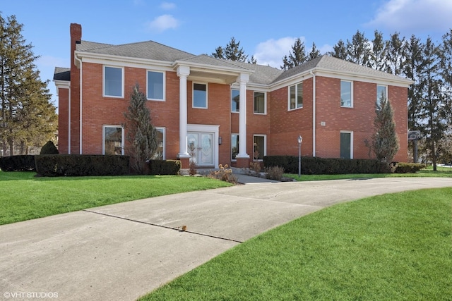 greek revival inspired property with brick siding, a chimney, and a front lawn