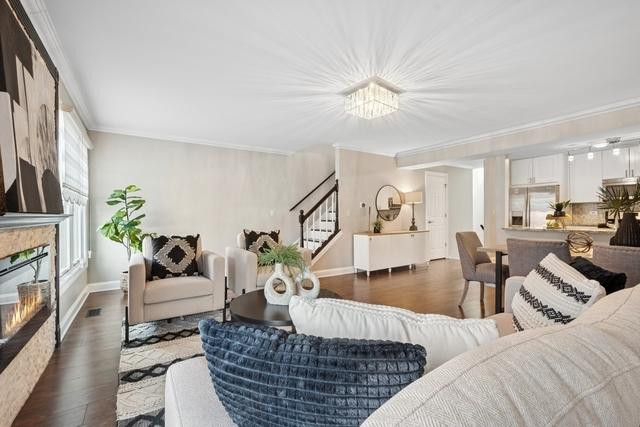 living area featuring wood finished floors, baseboards, stairway, a glass covered fireplace, and crown molding