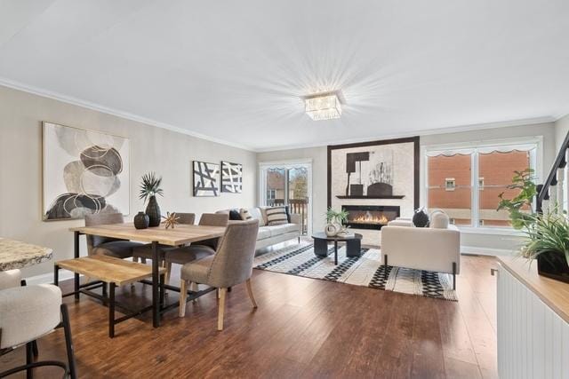 dining space featuring a glass covered fireplace, crown molding, and wood finished floors