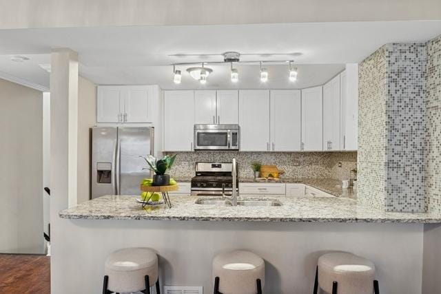 kitchen featuring light stone counters, a peninsula, a sink, appliances with stainless steel finishes, and tasteful backsplash