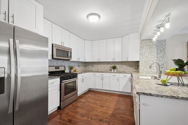 kitchen with tasteful backsplash, light stone counters, dark wood-type flooring, stainless steel appliances, and a sink