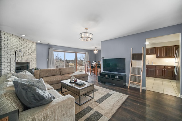 living area with an inviting chandelier, a brick fireplace, and light wood-style floors