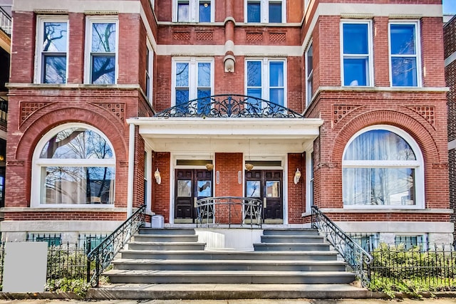 doorway to property featuring brick siding and fence