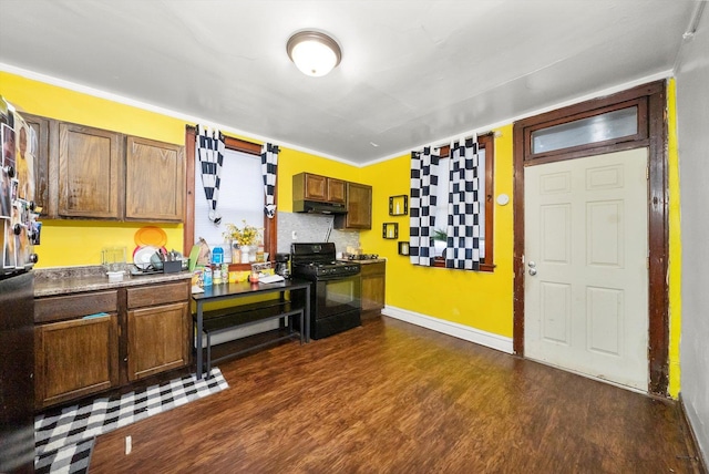 kitchen featuring baseboards, dark wood-type flooring, black gas range, and under cabinet range hood