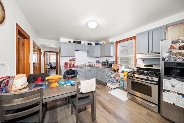 kitchen with decorative backsplash, light wood-style floors, stainless steel appliances, gray cabinetry, and under cabinet range hood