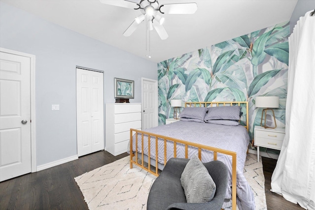 bedroom with an accent wall, ceiling fan, wood finished floors, baseboards, and wallpapered walls