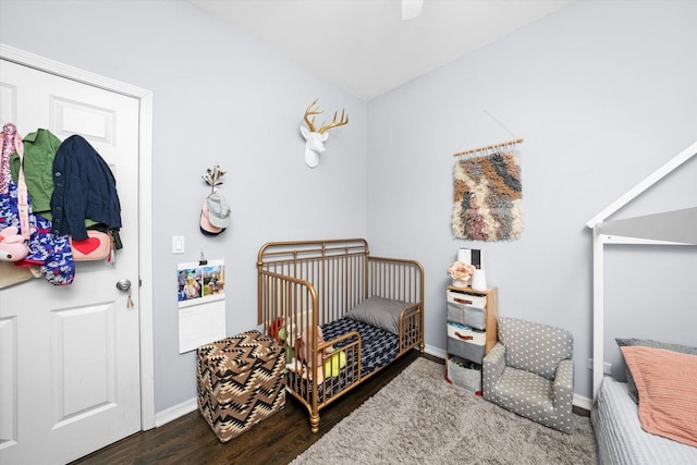 bedroom featuring a nursery area, ceiling fan, baseboards, and wood finished floors