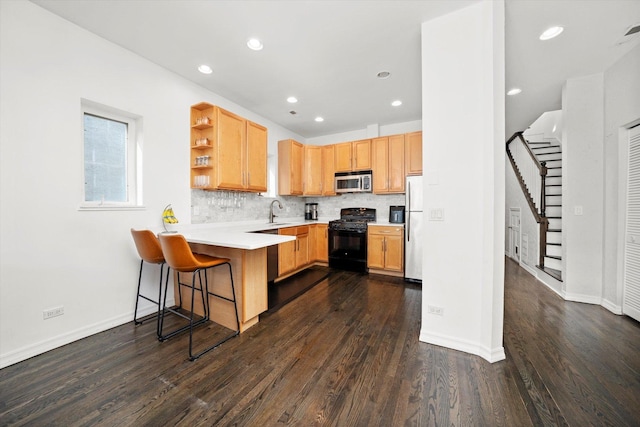 kitchen with black range with gas cooktop, a peninsula, a sink, freestanding refrigerator, and stainless steel microwave