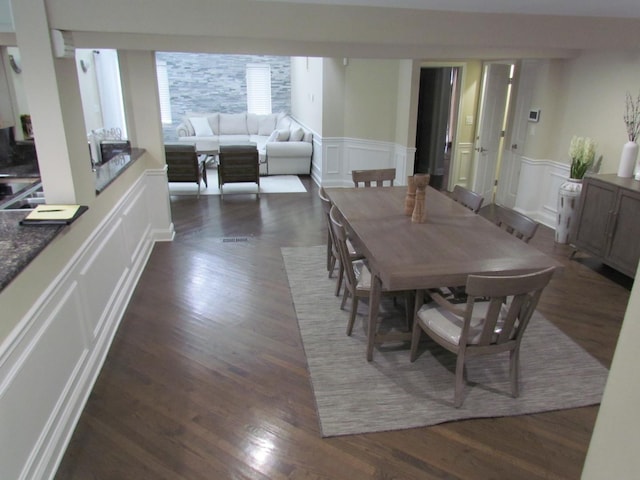 dining space with a decorative wall, wood finished floors, and wainscoting