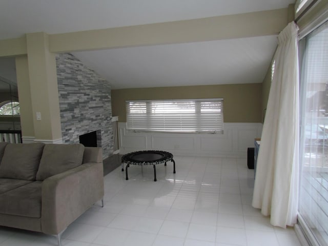 living room featuring vaulted ceiling, wainscoting, a fireplace, and a decorative wall