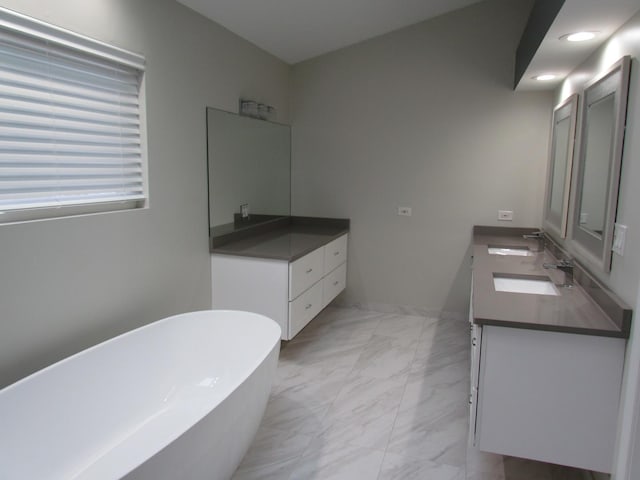 bathroom with double vanity, marble finish floor, a freestanding tub, and a sink