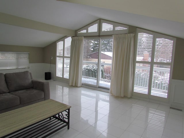 living room featuring lofted ceiling, wainscoting, and tile patterned floors