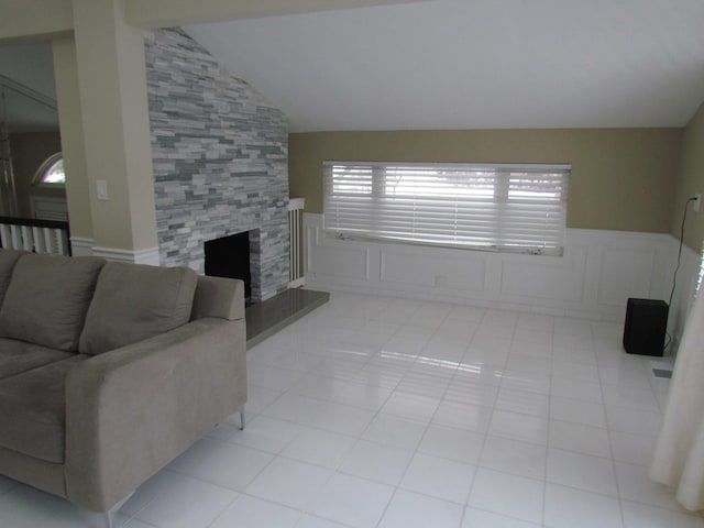 living room featuring lofted ceiling, wainscoting, a tile fireplace, and a decorative wall