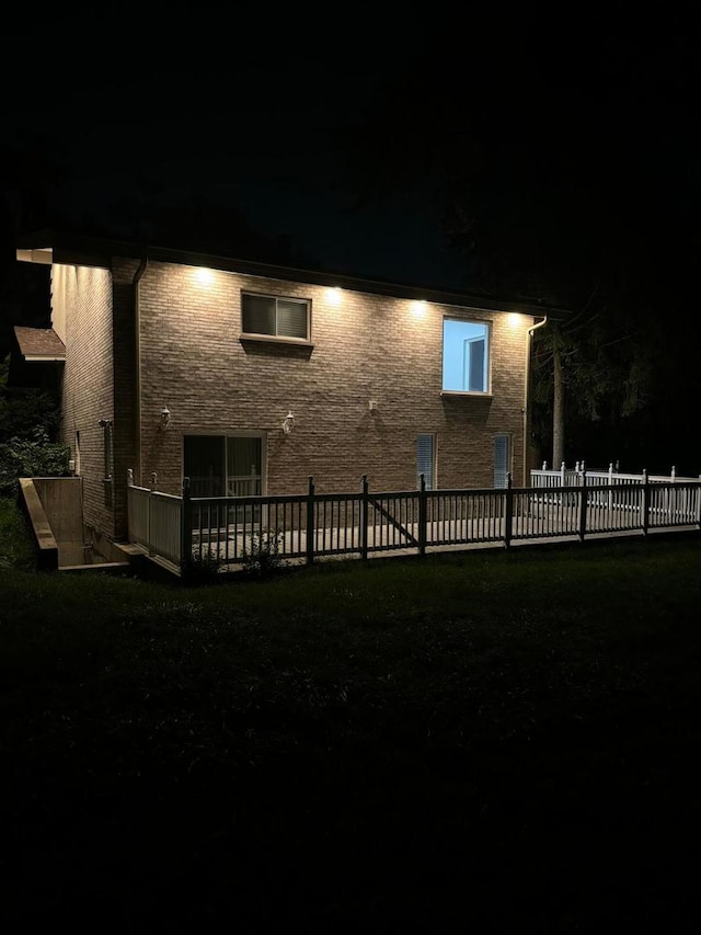 back of house at night featuring stone siding and fence