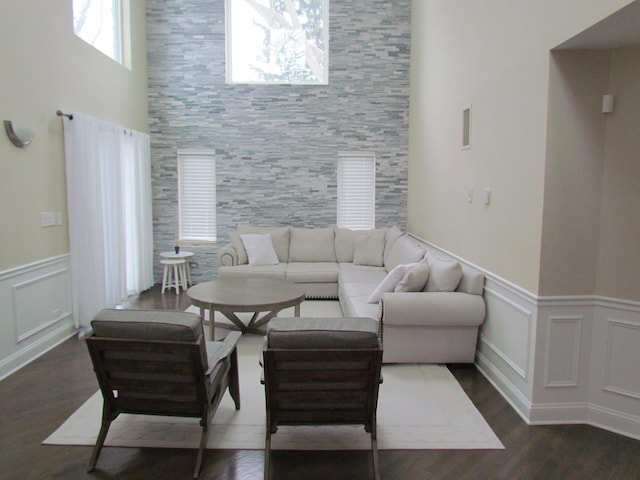 living room featuring a decorative wall, dark wood-style flooring, and wainscoting