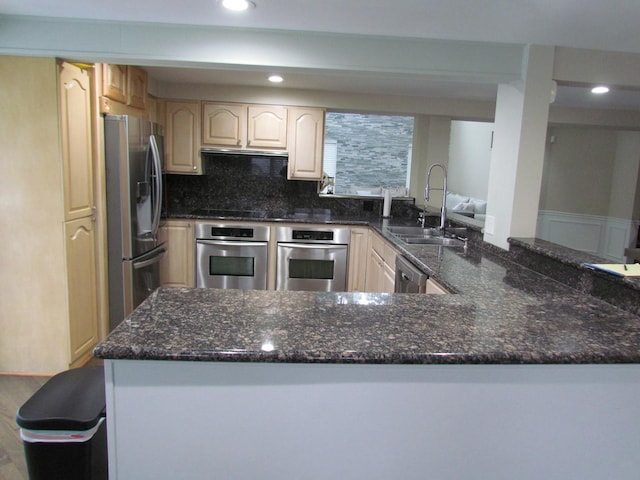 kitchen with backsplash, appliances with stainless steel finishes, a sink, dark stone countertops, and a peninsula