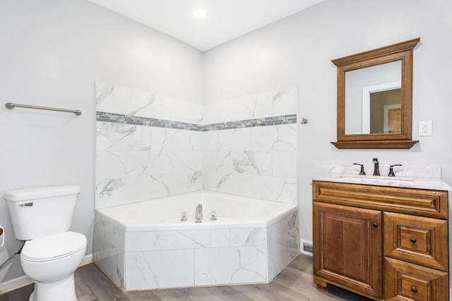 bathroom featuring vanity, wood finished floors, a tub with marble appearance, and toilet