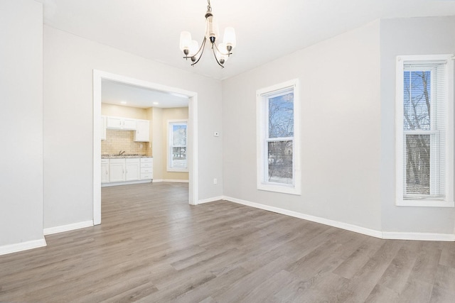 unfurnished dining area featuring light wood finished floors, baseboards, a sink, and an inviting chandelier