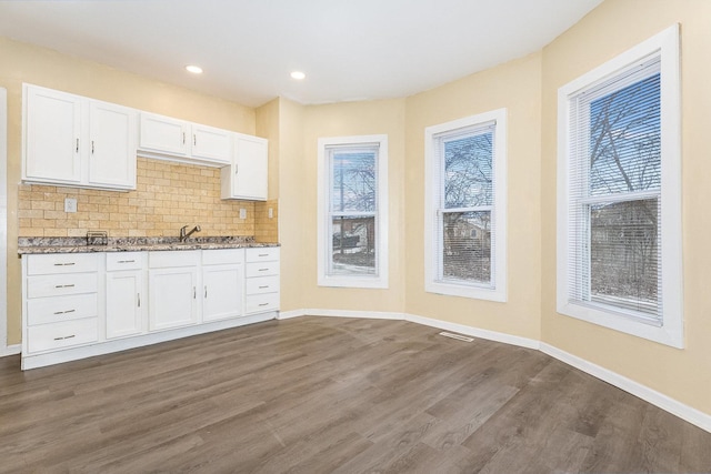 kitchen with baseboards, white cabinets, light stone countertops, tasteful backsplash, and dark wood finished floors