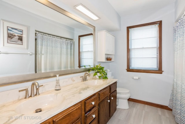 bathroom featuring double vanity, toilet, baseboards, and a sink