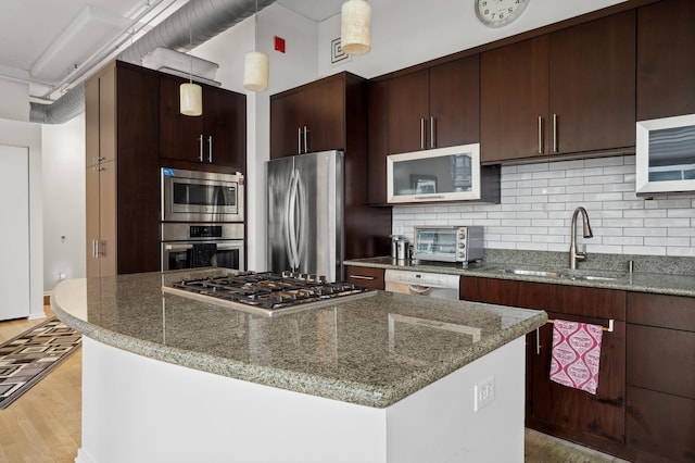 kitchen featuring appliances with stainless steel finishes, a kitchen island, a sink, and tasteful backsplash