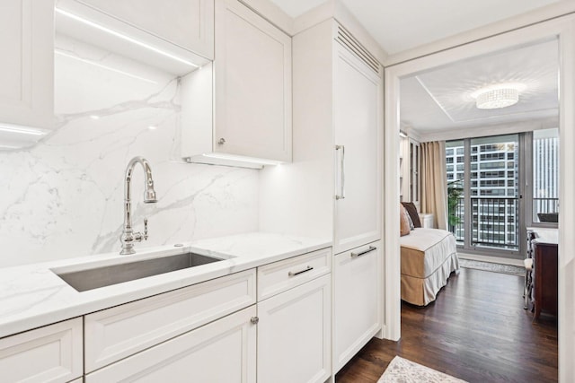 kitchen with light stone counters, dark wood finished floors, white cabinetry, and a sink