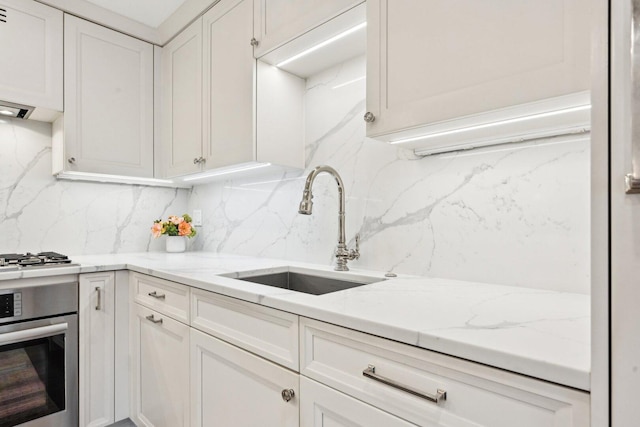 kitchen with appliances with stainless steel finishes, white cabinetry, a sink, and backsplash